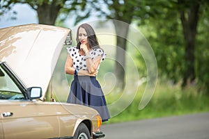 Woman in need for assistance desperately looking down to an open hood car engine after a breakdown