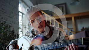 A woman is new to playing the guitar. She clumsily touches the strings and looks at the clues on the laptop