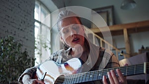 A woman is new to playing the guitar. She clumsily touches the strings and looks at the clues on the laptop