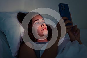 woman night owl succumbs to social media& x27;s allure, smartphone in hand, battling insomnia& x27;s grip