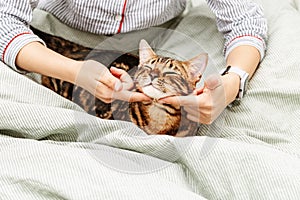 Woman in nightdress on bed stroking her darling Bengal cat. Pet in hands of hostess. Domestic cat