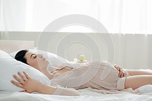 Woman in nightie touching tummy while sleeping in bed
