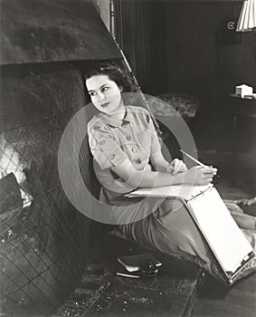 Woman with notebook daydreaming by fireplace