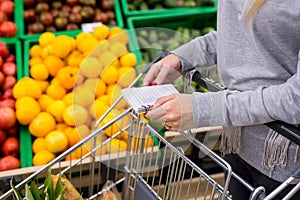 Woman with notebook in grocery store, closeup. Shopping list on paper.