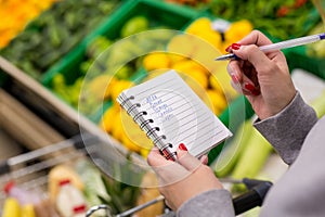 Woman with notebook in grocery store, closeup. Shopping list on paper.