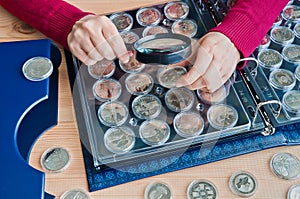 Woman-numismatist considers coins from the album for coins in capsules