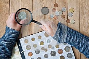 Woman-numismatist views coins from a coin album through a magnifying glass. Top view