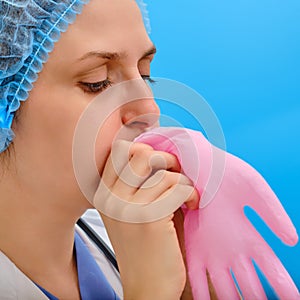 Woman nurse blows up a pink medical glove, close-up on a blue background. Doctor puff a protective glove with air, concept