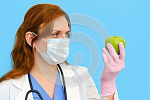 Woman nurse with green apple on a blue background, face closeup