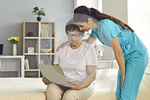 Woman nurse helping elderly lady patient with laptop at home lifestyle portrait