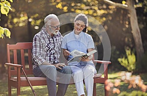 Woman nurse reading book to senior man in park