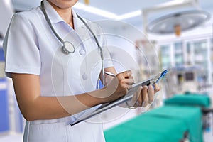 Woman nurse in white coat report in a notebook on blur background of operating room, clipping path included