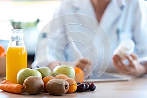 Woman nutritionist doctor writes the medical prescription for a correct diet on a desk with fruits, pills and supplements