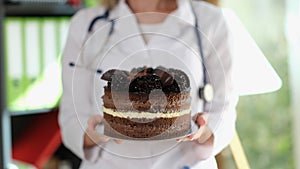 Woman nutritionist holds large chocolate cake in her hands.