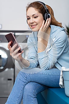 woman occupied on smartphone while waiting for washing in launderette photo