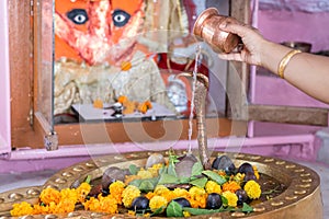 woman offering holy water to hindu god shivalinga worshiped with flower and bell paper at temple