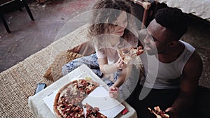 Woman offers pizza to man, but eat slice by herself. Multiracial couple having fun during the meal with fast food. photo