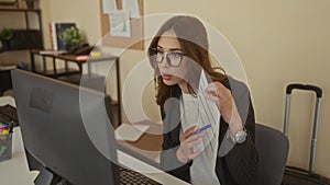Woman in office analyzing document at desk with computer suitcase in background and glasses focus