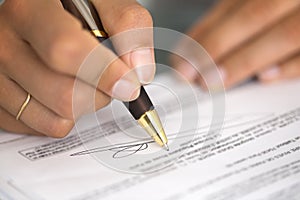 Woman at office desk signing a contract with shallow focus on si