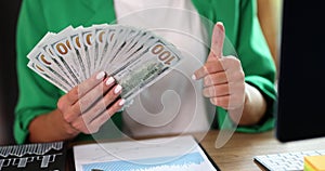 A woman in the office holds dollars in a fan, hands close-up