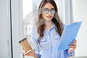 A woman in the office near the window, holding documents in her hands