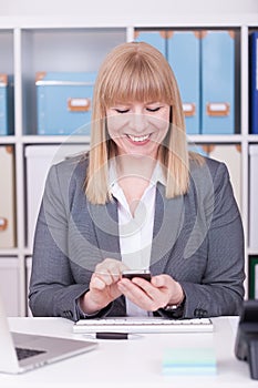 Woman at the office typing and messaging with her mobile phone