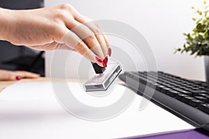 Woman at office work. Woman stamps documents at the desk. A female hand with red nails in the office scenery