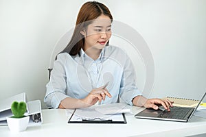 Woman office worker reading and typing business project report on laptop after that taking note of information