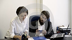 Woman, office worker shows important documents to her bearded boss who is busy with playing smart phone games in the