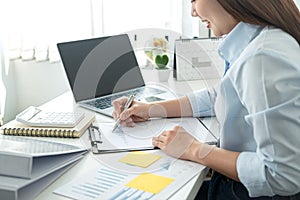 Woman office worker sitting to working and writing business project report on clipboard during checking information