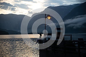 woman at old wooden pier looking at sunset over hallstatt sea lake