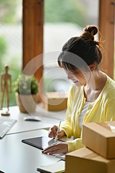 Woman online seller using digital tablet for confirming orders or taking orders from customer.