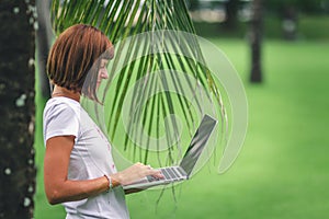 Woman online shopping concept. Woman in the green park with modern laptop. Bali island.