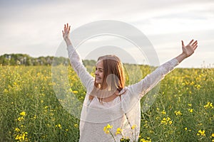 Woman with open arms in the green rapseed field at the morning