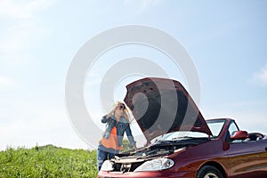 Woman with open hood of broken car at countryside