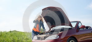 Woman with open hood of broken car at countryside