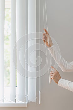 Woman open white fabric vertical jalousie in room