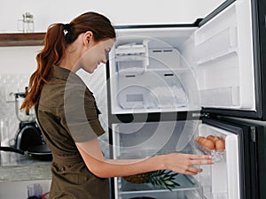 A woman opened the refrigerator smiles looking into it, thinking what to cook, defrosted the refrigerator, freezer