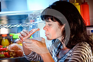 Woman opened the refrigerator and sniffs a container of food