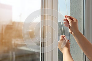 Woman opening blinds on window indoors, closeup. Space for text