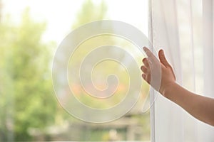 Woman opening curtain indoors, closeup. Space for text