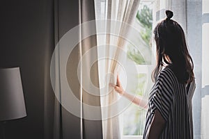 Woman opening curtain looking through window