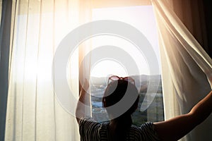 Woman is opening the curtain at the window in the morning
