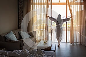 Woman opening curtains in hotel room in the morning