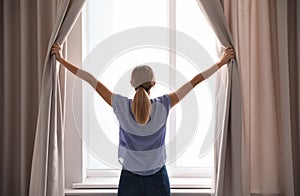 Woman opening curtains and looking out of window