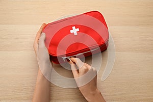 Woman opening first aid kit bag at light wooden table, top view