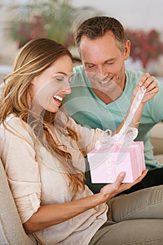 Woman opening gift, man and happy with surprise for birthday or anniversary, love and support with romance. Couple in