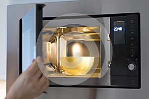Woman opening microwave door with yellow soup bowl inside photo