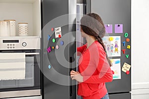Woman opening refrigerator door with child`s drawings, notes and magnets