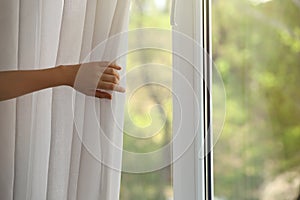 Woman opening white window curtains in room, closeup. Space for text